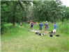 Four men at disc golf stand one throwing